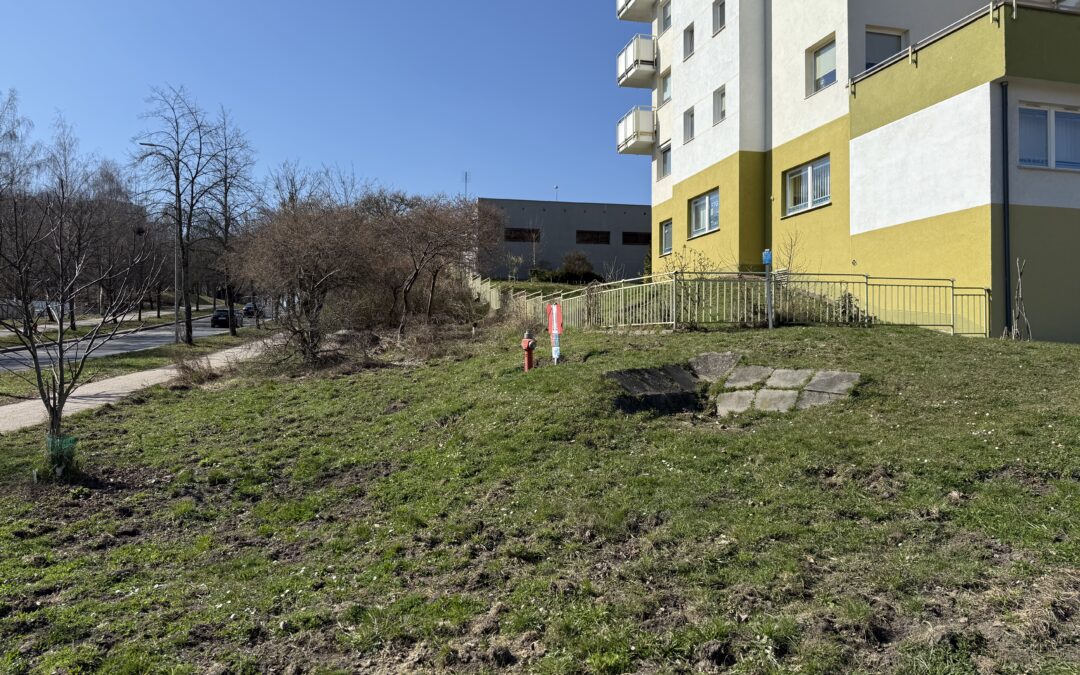 Zdjęcie terenu przy budynku mieszkalnym – niezagospodarowana działka z trawnikiem, chodnikiem oraz elementami infrastruktury technicznej, widok na otoczenie inwestycji.