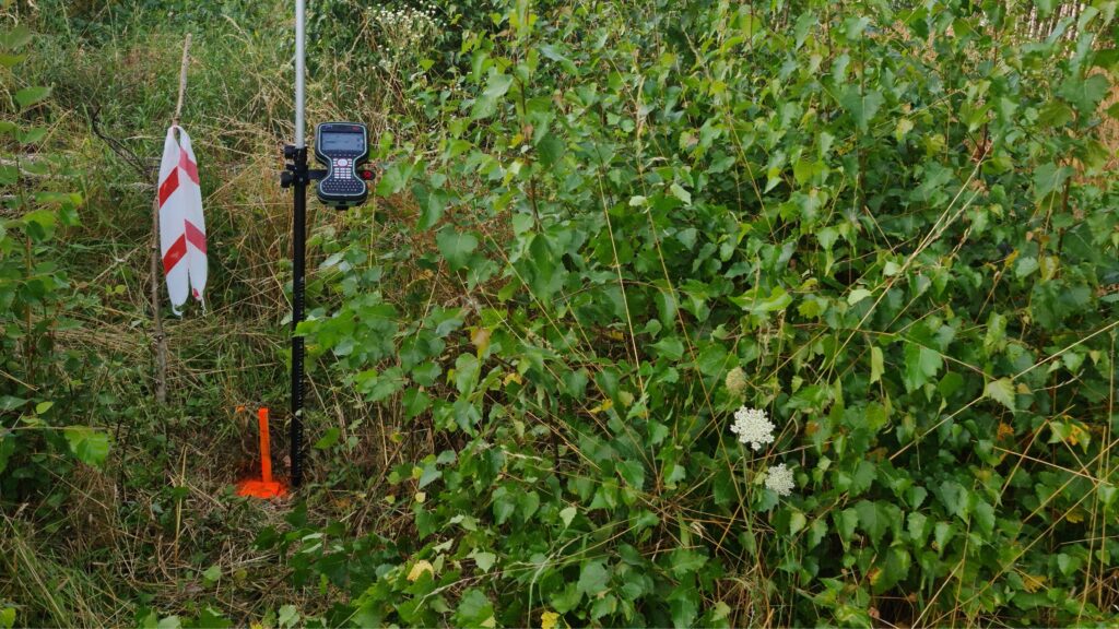 Punkt graniczny działki w terenie – oznaczenie granicy palikiem oraz pomiar geodezyjny wykonany przy użyciu odbiornika GPS w zarośniętym terenie.